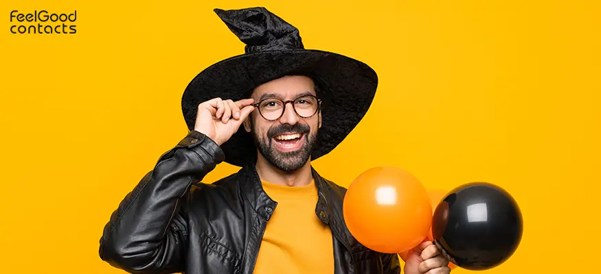 Man wearing Halloween costume with witch hat, glasses and black and orange balloon